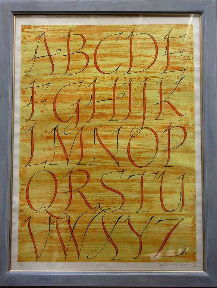 A hand written alphabet. The letters are all in a slim curving uppercase, orange on a yellow background. 