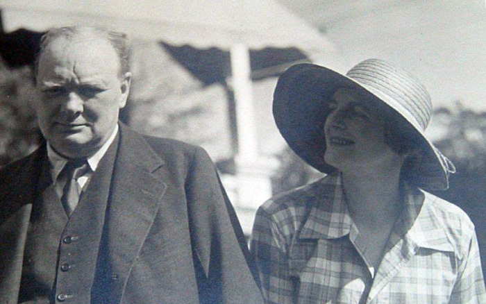 Black and white photo of Winston and Clementine Churchill in the Bahamas. Clementine is wearing a large sun hat and is smiling at Winston, who is looking at the camera.