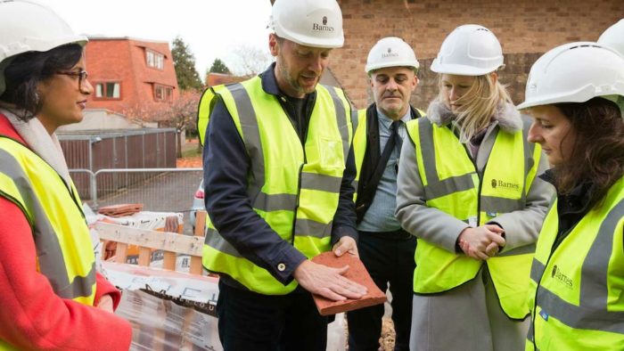 A group of College staff being shown a terracotta tile outside the new graduate housing.