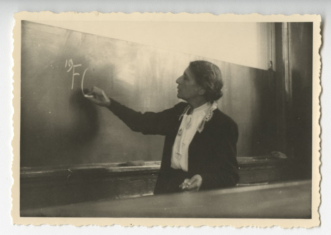 Black and white photograph of Lise Meitner writing an equation on a blackboard