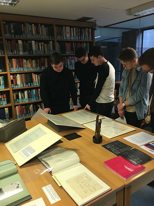 A group of 5 pupils gathered around a table in the Archives Centre reading room, examining documents that have been laid out.
