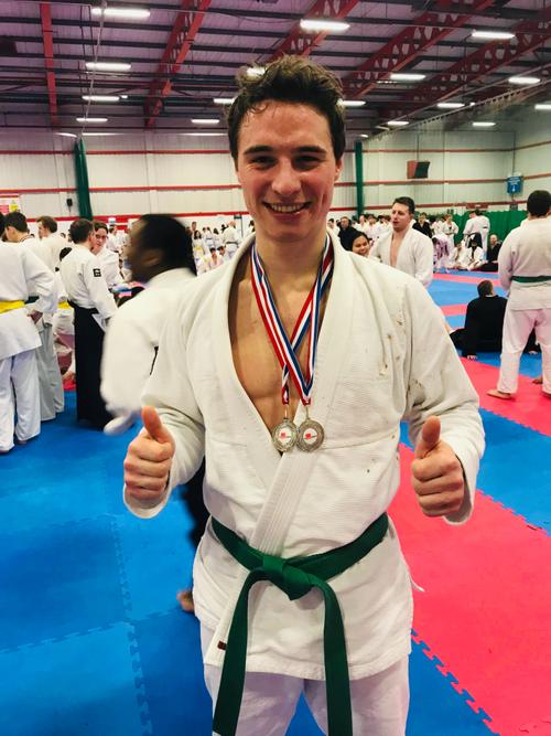 Michele Blago giving two thumbs up to the camera. He is wearing a jiu-jitsu uniform and has 2 silver medals around his neck.