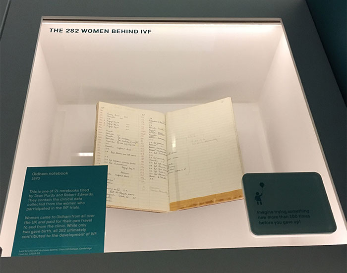 Edwards' notebook on display in a glass exhibition case. The case is captioned "the 282 women behind IVF"
