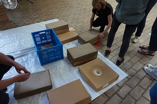 A variety of cardboard archival boxes laid out on a white sheet. Some are visibly waterlogged while others are just a bit damp. Staff are gathered around, examining them.