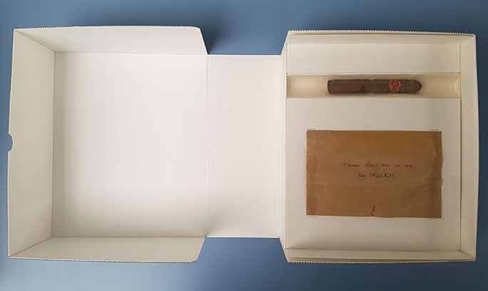 An open clamshell box with the cigar and an envelope in their newly constructed housing.