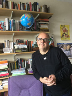 Profile photo of Stephen Meredith leaning on a desk, with a bookcase in the background