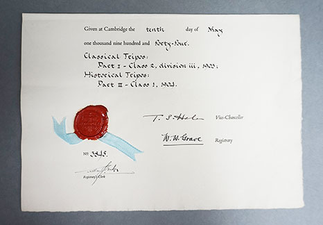 A Cambridge graduation diploma which has been folded in half, the end of the document is visible which has a blue ribbon attached with a red wax seal.