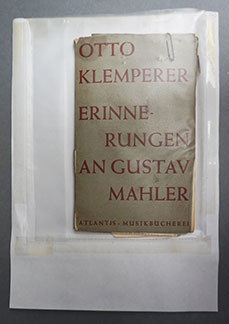 A plastic wallet containing a small book 'Otto Klemperer Erinne Rungen An Gustav Mahler'. There is a paperclip attached to the top edge of the front cover of the book