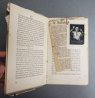 An open book with a newspaper clipping and a small photograph paperclipped to one of the pages