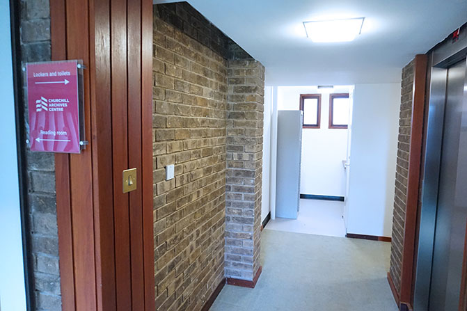 The landing outside the Archives Centre reading room post-refurbishment. The door at the far end of the corridor has been removed, letting light into the corridor from two windows in the room beyond. The lockers have moved into the room at the end of the corridor.