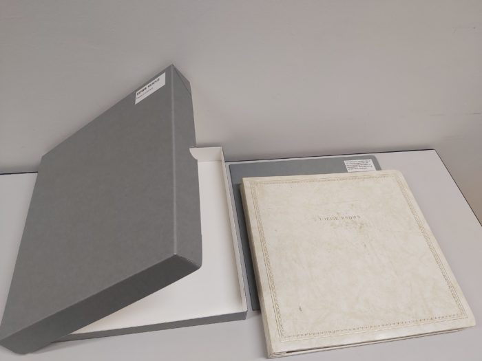 A grey archival clamshell box, which has been custom-made to fit the cleaned and restored photo album which lies next to it on the work surface.