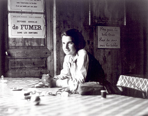 Black and white photo of Rosalind Franklin leaning on a table inside a French hotel or restaurant