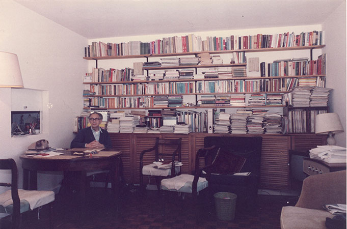 Mark Abrams seated at a table, looking at the camera. The wall behind him is filled with bookshelves.