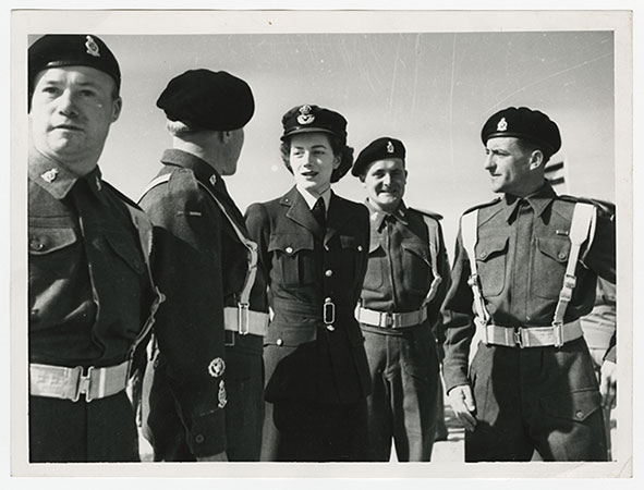 Black and white photograph of Sarah Churchill in Women’s Auxiliary Air Force uniform, standing amongst a small group of male RAF pilots