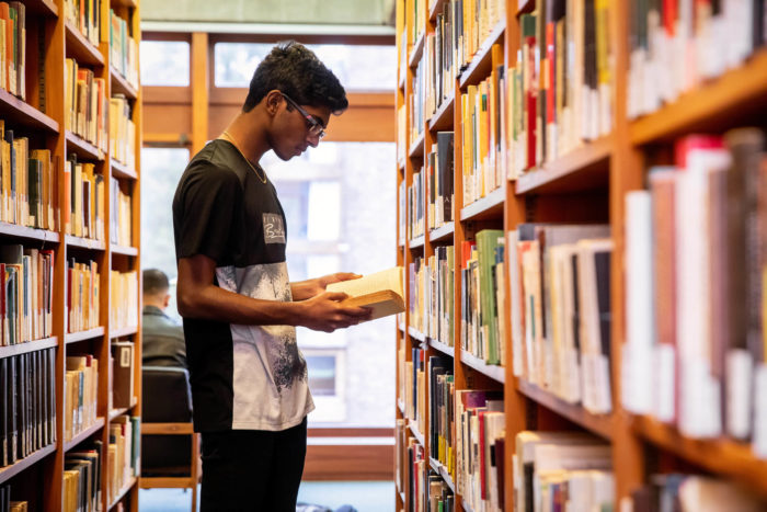 Male student reading a book in the library stacks.