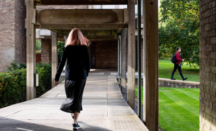 A woman walking away from the camera in the College grounds. A man is walking further along the path in the background