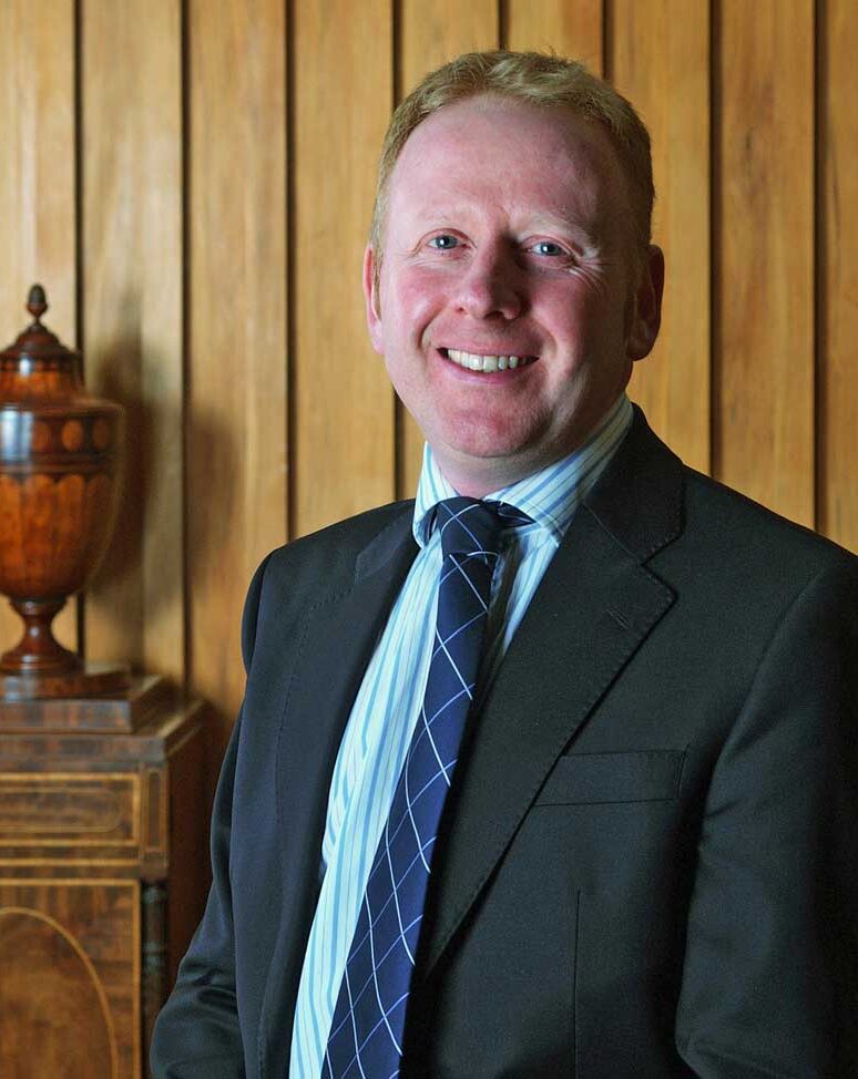 Profile photo of Alex Webb. He is standing in a wood panelled room and smiling at the camera.