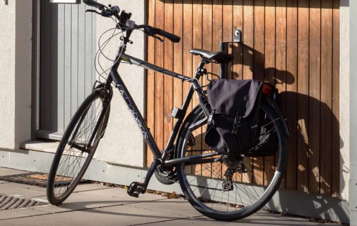 A black bicycle with panniers leaning against the wall of a postgraduate flat.
