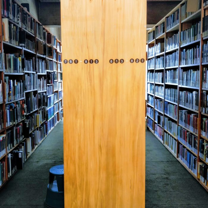 The end of a row of bookshelves in the College Library. The end of the shelf is labelled with the classmarks of that section.