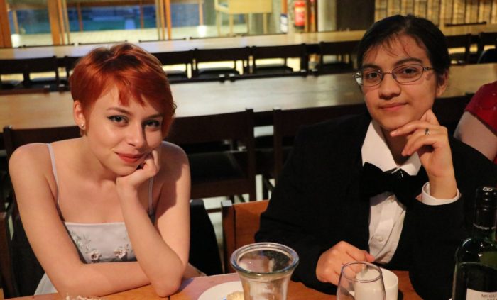 2 students in formal attire at a Formal Hall. They are seated at a table and are smiling up at the camera.