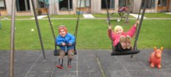 Two young children on the swings in the playground outside the Wolfson Flats