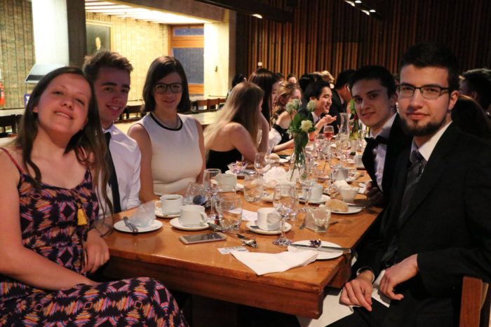 A group of students at formal hall dinner, they are turning to smile at the camera.