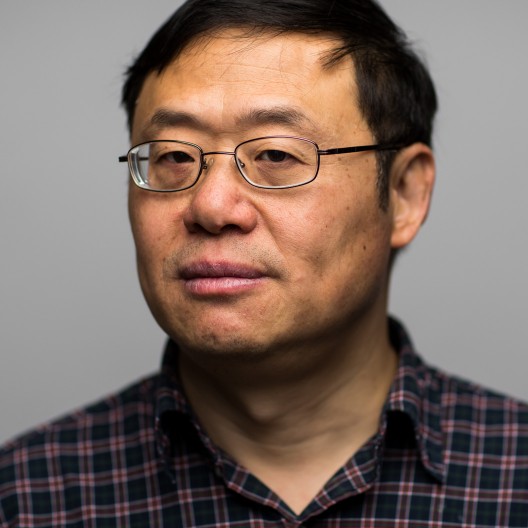 Professor Qiang Fu looks back at the camera with his head turned to his right. He is wearing glasses and an open neck checked shirt.