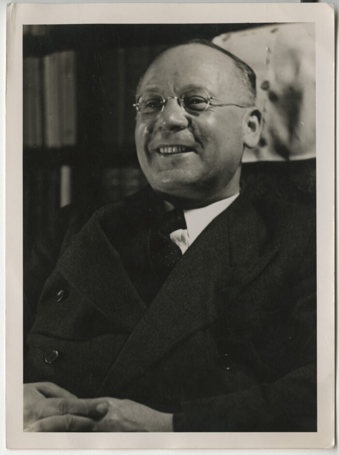 Black and white half length photograph of Hersch Lauterpacht, leaning back in his chair and smiling