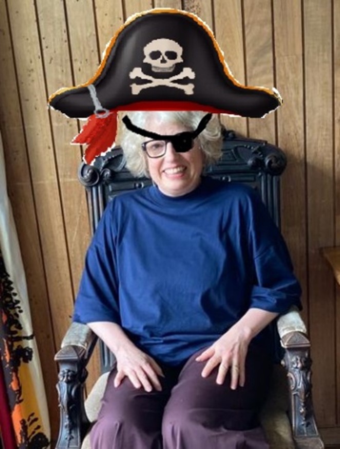 Half length colour photograph of Vicki Thoms sitting in a chair, wearing a pirate hat and eye patch