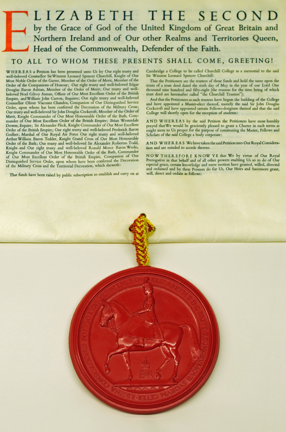 A large official document featuring an ornate heading in uppercase, Elizabeth the Second, and formal text below. Attached at the bottom is a red wax seal with the image of a mounted figure, connected by a braided yellow cord.