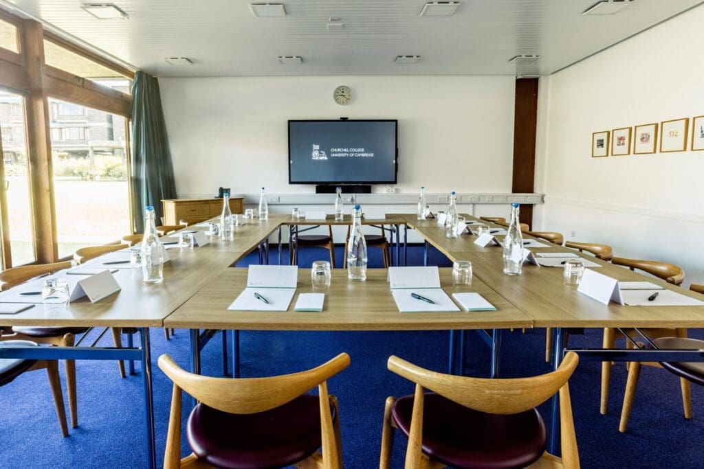 A conference room with a U-shaped table setup. Chairs surround the table, which has name cards, notebooks, water bottles, and glasses on it.