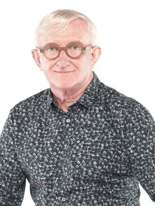 Man with short white hair and round glasses, wearing a patterned dark shirt with a subtle floral design, smiles at the camera against a white background.