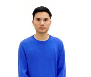 Person wearing a blue sweater stands against a plain white background, looking directly at the camera.