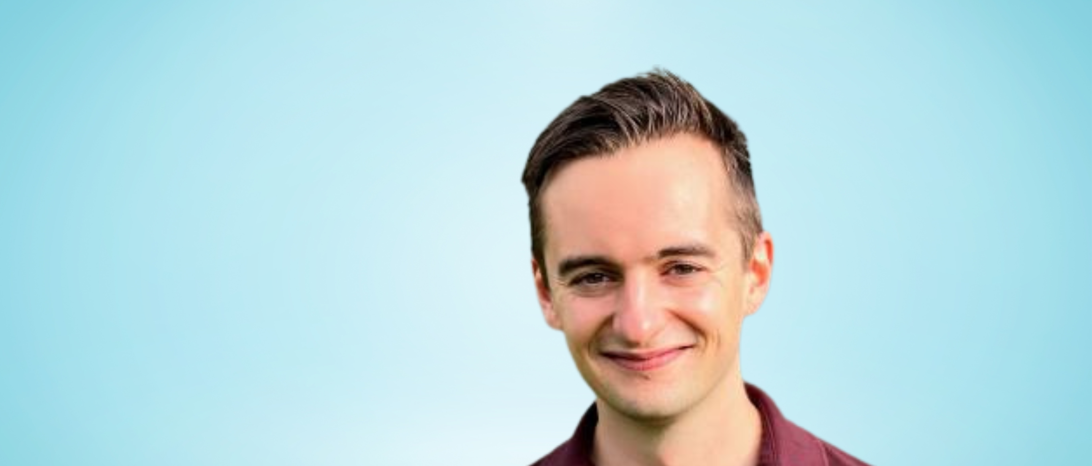 Man with short, dark hair and a maroon shirt smiling against a light blue background.